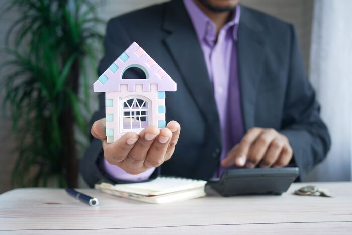 The featured image for the article titled: "tax tips for property investors: granny flats and cgt". The image includes a man in a suite holding a mini house out in his house.