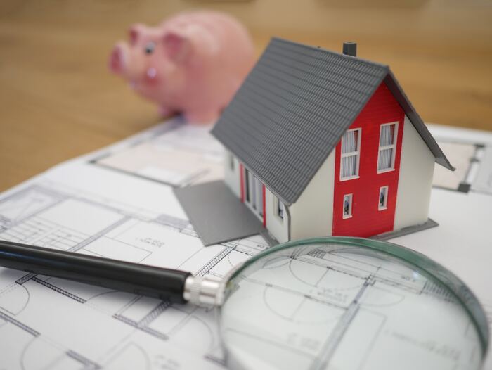 The featured image for the article titled: "Tax tips for property investors rental income explained". The image includes a magnifying glass, a mini house and a piggy bank sitting on top of a tax sheet.